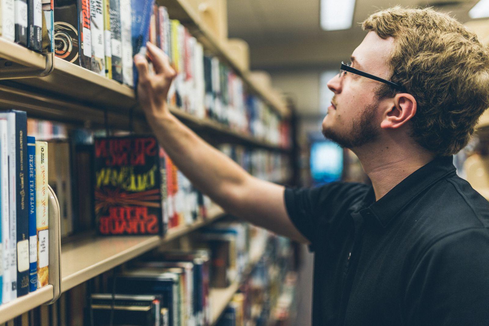 Male student searching through library stacks